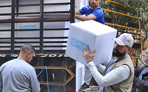 Group of men helping unload boxes of Plan supplies for a community